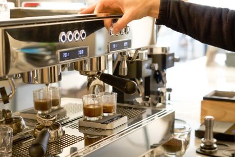 Hand ready to stop an espresso shot pulling on a Rocket espresso machine, with a scale showing the weight in grams