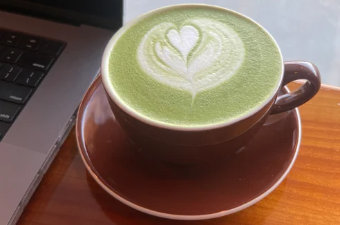 Matcha latte with tulip latte art in a brown cup on a wooden table